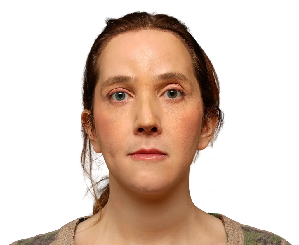 Front-facing woman with brown hair and a neutral expression, wearing a camouflage sweater against a black background
