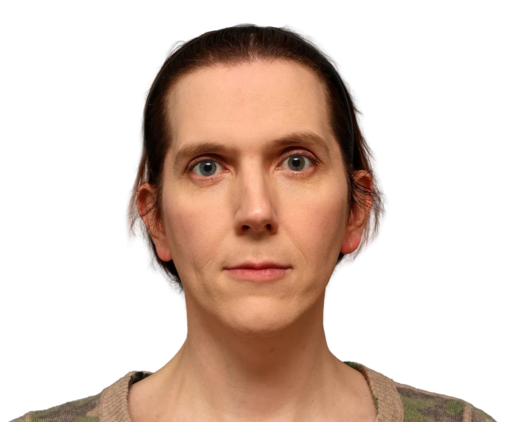 Close-up of a woman with blue eyes and brown hair pulled back by a black headband, wearing a camouflage sweater and a neutral expression.