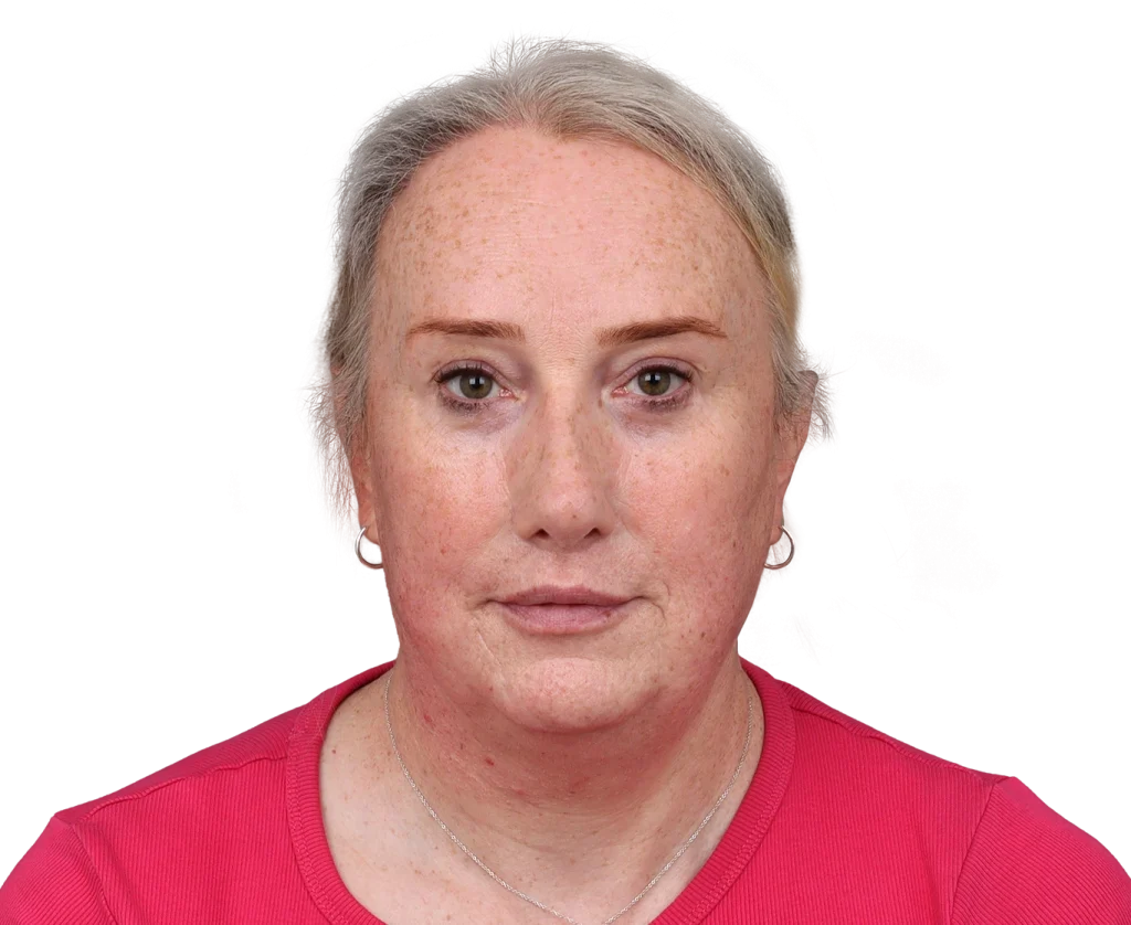 Portrait of a middle-aged woman with short gray hair, freckles, wearing a pink shirt, looking at the camera.