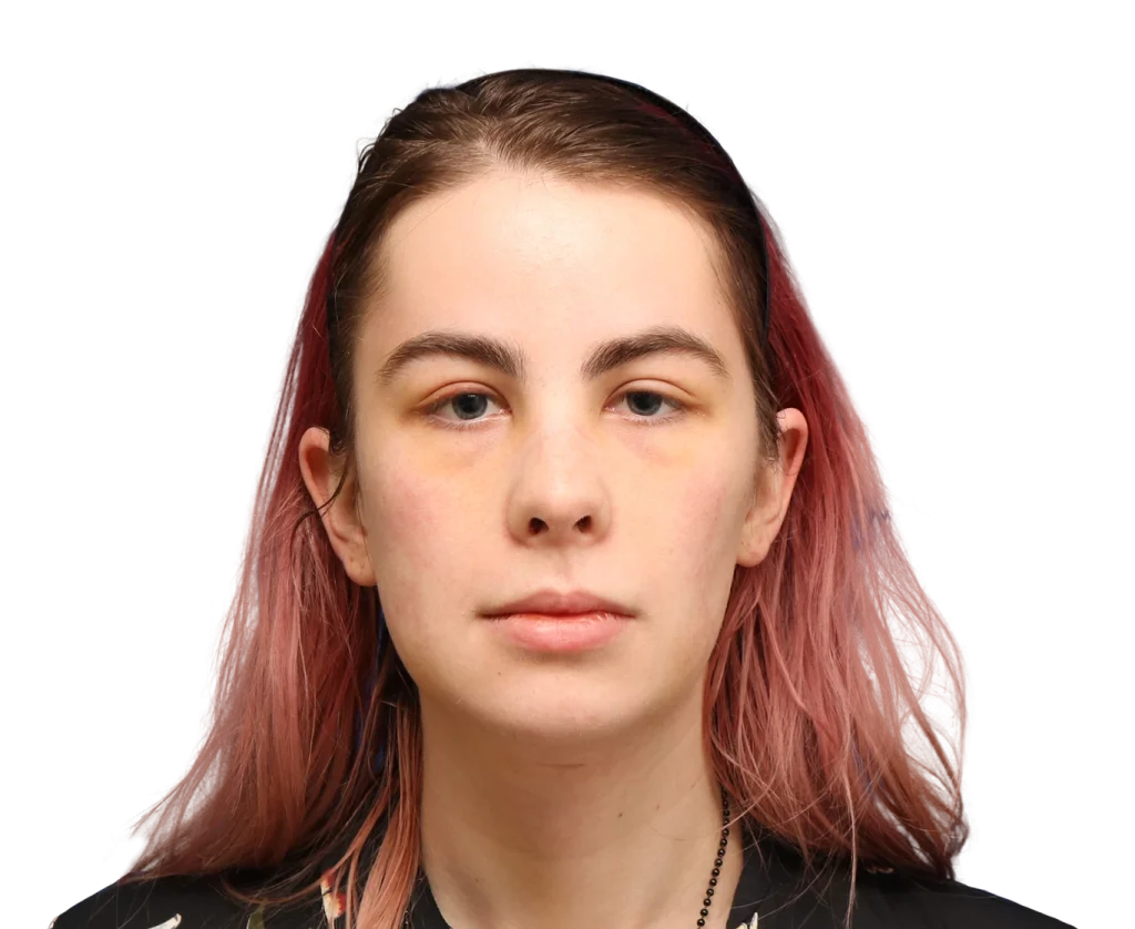 Close-up portrait of a young Elléonore with pink-tinted hair, facing the camera with a neutral expression against a dark background.
