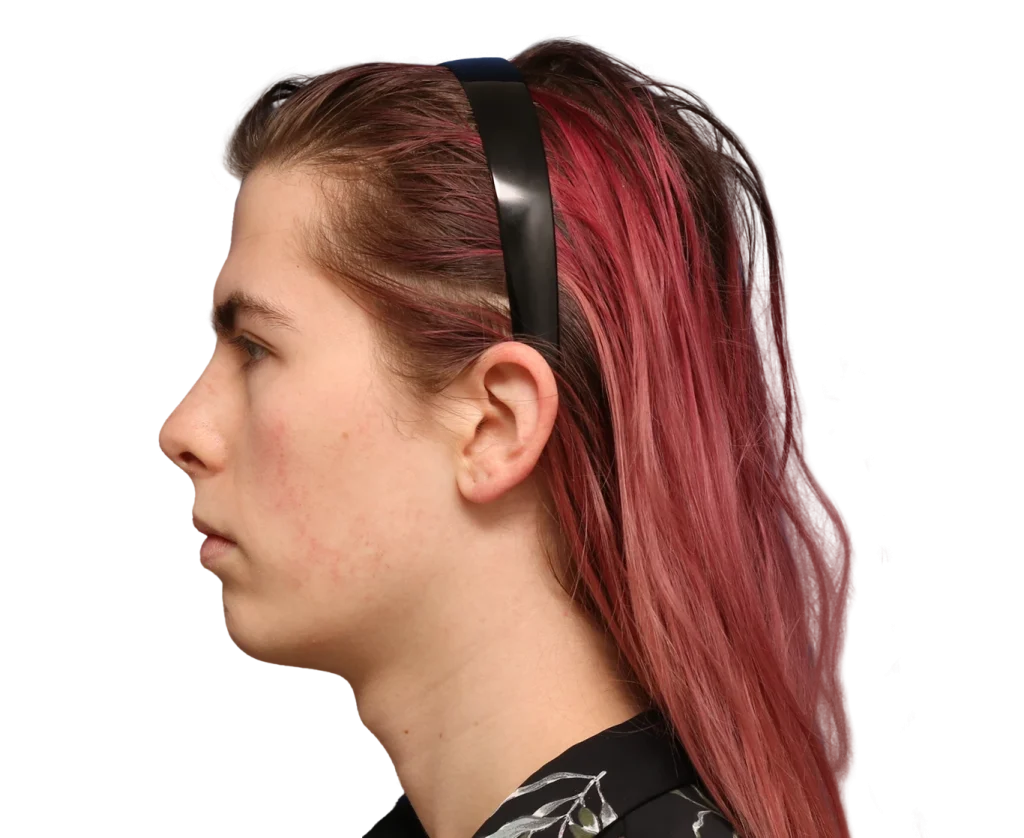 Profile of a young Elléonore with pink hair and black headphones, facing left