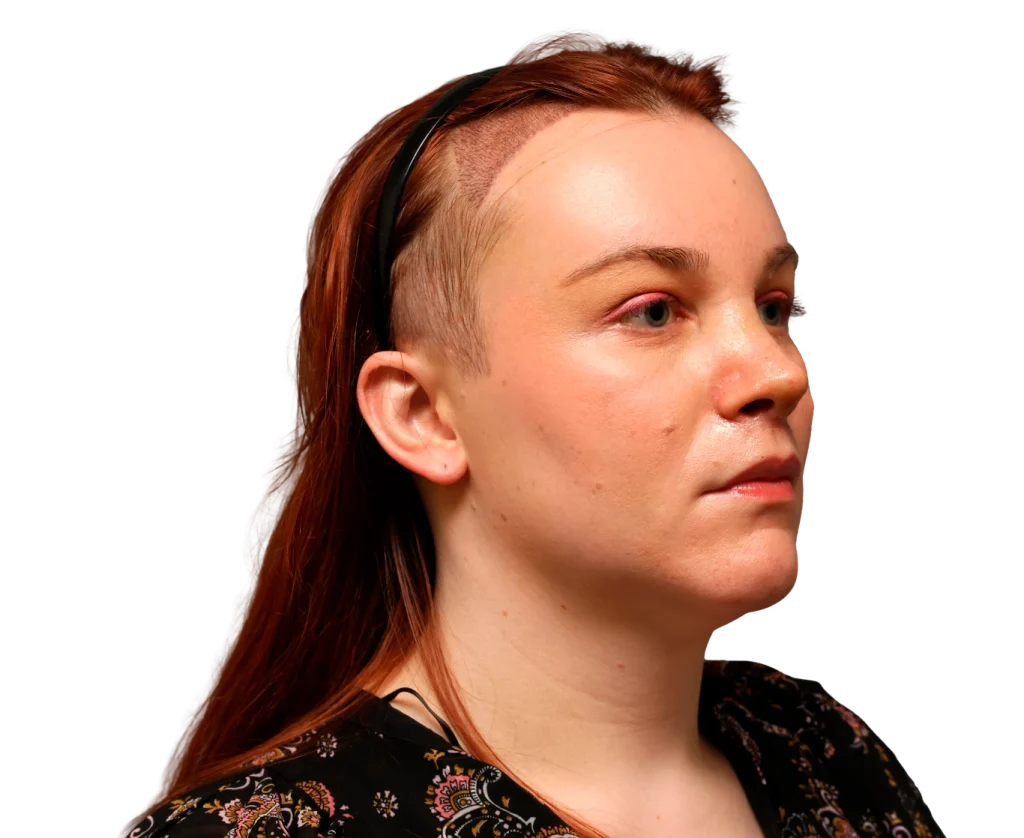 Person with a shaved-side hairstyle and long red hair, wearing a black headband, looking to the right.