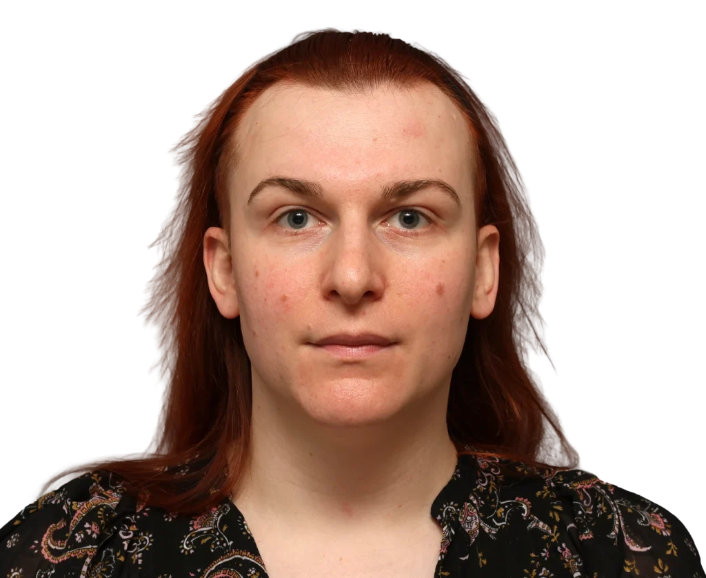 Front-facing portrait of Mia with red hair, light skin, and a neutral expression, wearing a patterned blouse against a dark background.