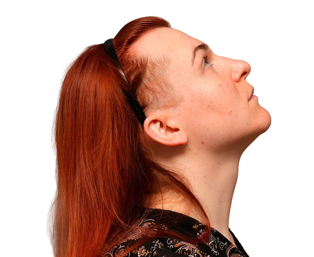 Mia with red hair in a side profile, looking upward, head tilted back, wearing a patterned top and a black hair tie.