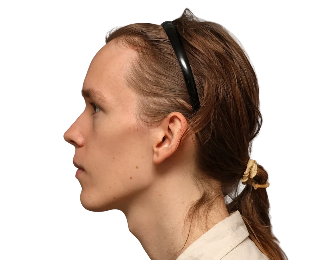 Profile of Zoey facing left wearing a black headband, light brown hair tied back with a scrunchie, neutral expression