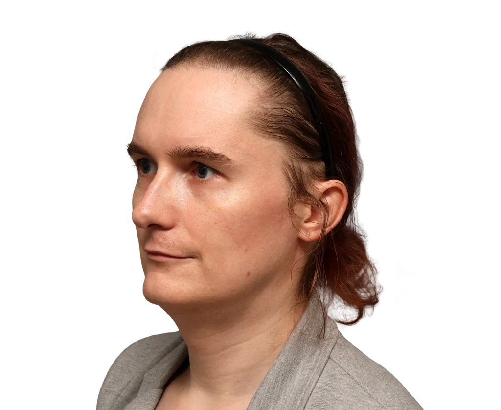 Side portrait of a woman with light skin, blue eyes, and brown hair pulled back with a black headband, wearing a gray blazer.