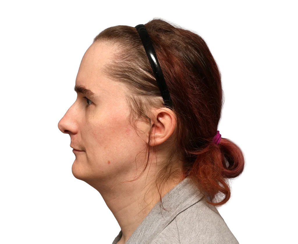 Side view of a woman with a black headband, tied-back reddish hair, and a light grey blazer. (Informative: portrait of a woman wearing a headset accessory.)