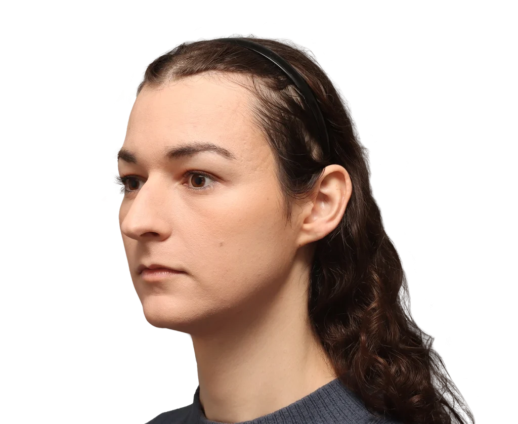 Side profile of a young woman with dark hair pulled back by a black headband, wearing a gray sweater, neutral expression against a black background